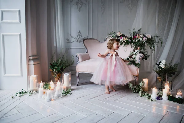 Çiçekler ve mumlarla süslenmiş beyaz bir stüdyo odasında pembe güzel elbiseler içinde güzel mutlu küçük bir kız.