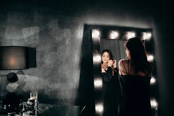 美丽的女人呆在大镜子旁边 黑暗的房间里挂着灯泡 — 图库照片