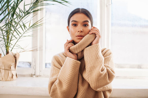 красивая женщина в свитере днем остается у окна 