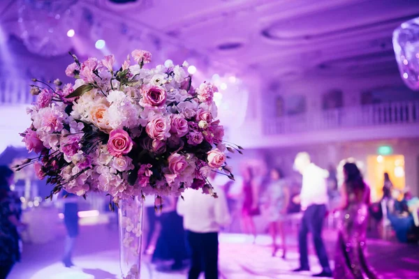 Lüks bir düğün odasının içinde çiçekler ve arka planda dans eden insanlar.