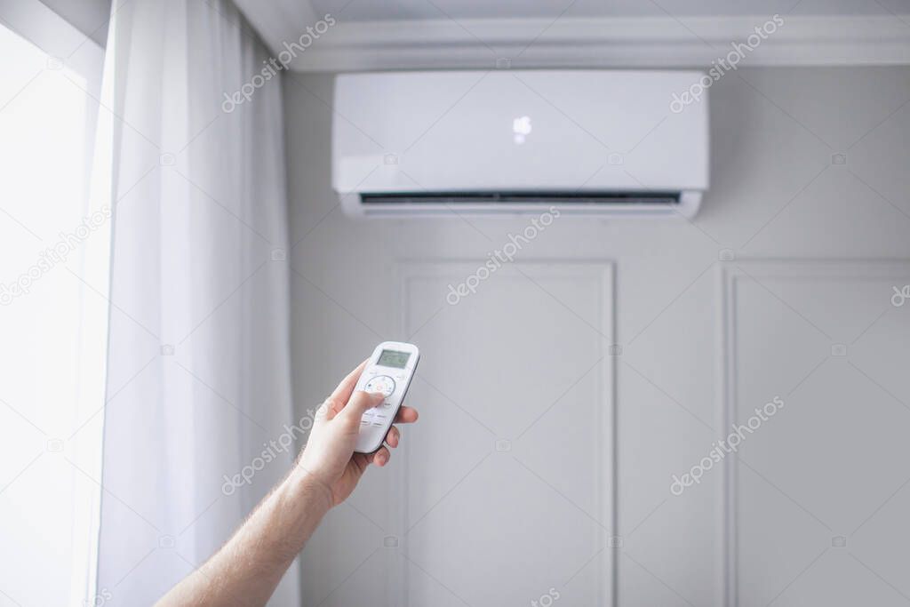 Air conditioner inside the room with hand operating remote controller in beautiful room, gray wall