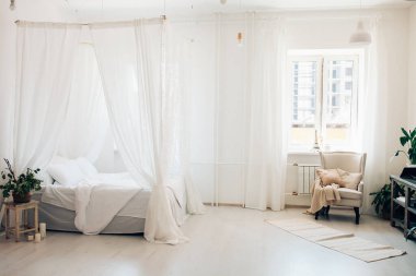 Minimalist İskandinav tarzı bir yatak odasında rahat bir yatak odası, örtülü yatak, battaniye yastıkları, bitki. Günaydın güneşli fotoğraf.