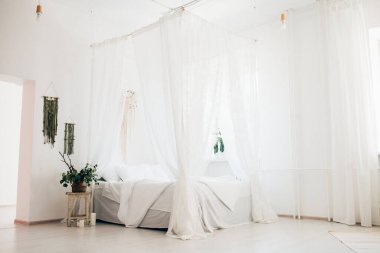 Minimalist İskandinav tarzı bir yatak odasında rahat bir yatak odası, örtülü yatak, battaniye yastıkları, bitki. Günaydın güneşli fotoğraf.