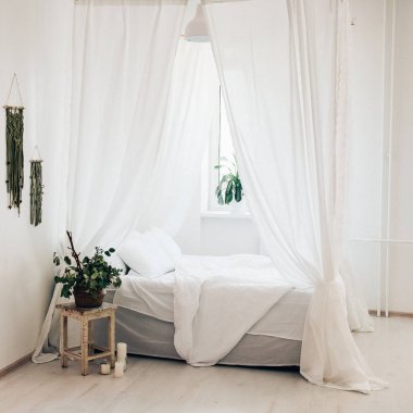 Minimalist İskandinav tarzı bir yatak odasında rahat bir yatak odası, örtülü yatak, battaniye yastıkları, bitki. Günaydın güneşli fotoğraf.