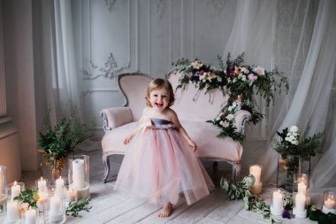Çiçekler ve mumlarla süslenmiş beyaz bir stüdyo odasında pembe güzel elbiseler içinde güzel mutlu küçük bir kız.