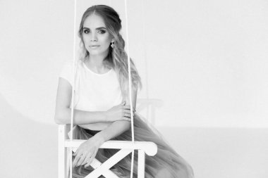 Şık etekli ve bluzlu güzel sarışın manken ahşap salıncakta oturuyor.