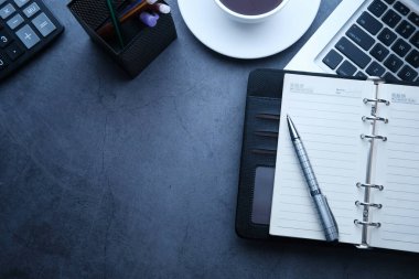 Gri arkaplanda dizüstü bilgisayar, hesap makinesi ve not defterinin yüksek açılı görünümü 