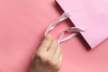 Kadın eli pembe arka planda kağıt alışveriş torbası. 