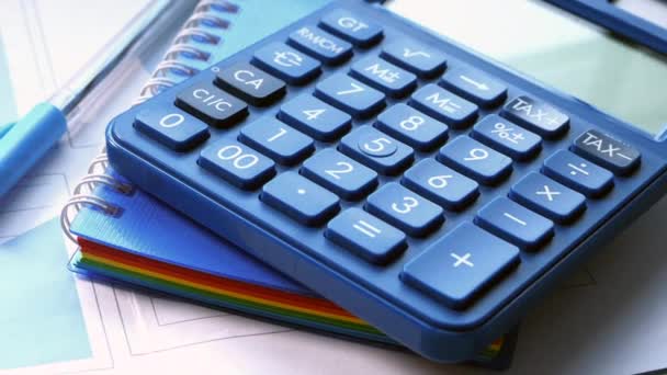 Close-up van blauwe rekenmachine en financiële grafiek op tafel. — Stockvideo