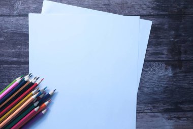 Ahşap zemin üzerinde renkli kalemler olan boş kağıt 