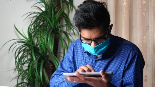 Hombre joven feliz en la máscara facial que trabaja en la tableta digital — Vídeo de stock