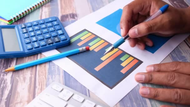 Young man hand with pen analyzing bar chart on table — Stock Video