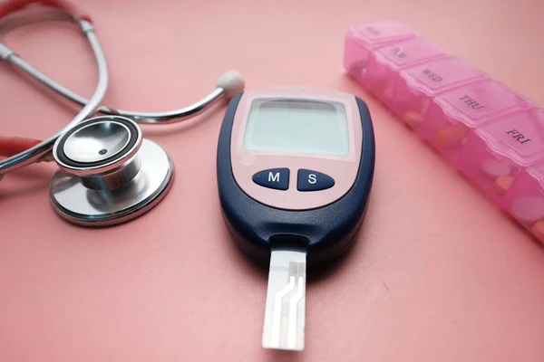 Medidores de glicose no sangue, estetoscópio e caixa de pílulas em rosa — Fotografia de Stock