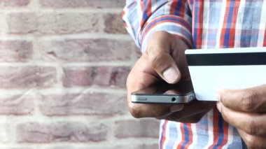 Adamın biri kredi kartını tutuyor ve online akıllı telefon alışverişi yapıyor. 