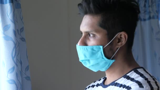 Een jonge aziatische man masker op zijn gezicht kijkend door het raam — Stockvideo