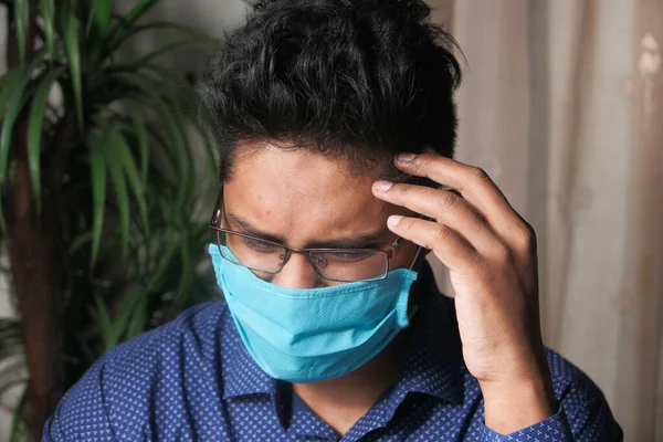 Μια νεαρή ασιατική μάσκα στο πρόσωπό του που υποφέρει από πονοκέφαλο. — Φωτογραφία Αρχείου
