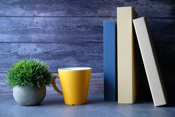 Kitap yığını, kahve kupası masanın üstünde. 