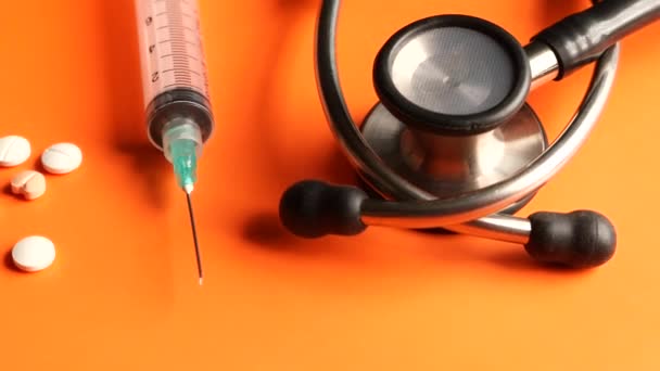 Piller, stetoskop och spruta på orange bakgrund — Stockvideo