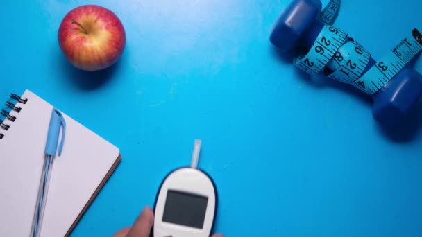 Mierniki poziomu glukozy we krwi, notatnik i jabłko na niebieskim biurku — Wideo stockowe