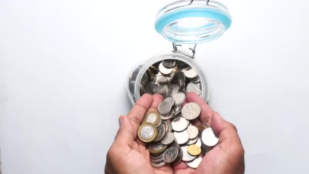 Man pouring coins into glass jar on table. — Stock Video