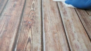 Mavi eldivenli bir adam ahşap yüzeyi temizliyor. 