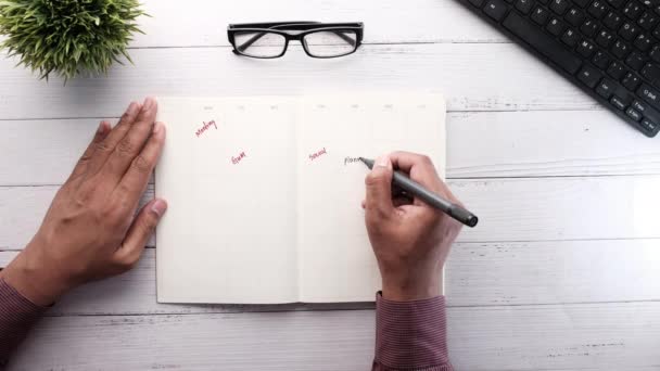 Рука людини, що пише плани на блокноті на столі . — стокове відео