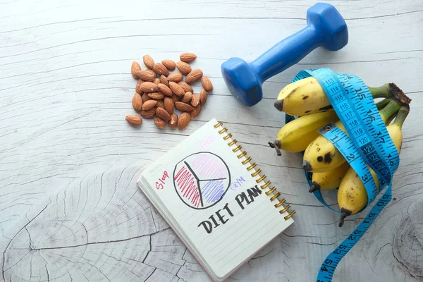 Диетический план с миндальным орехом, гантели, банан на столе . — стоковое фото