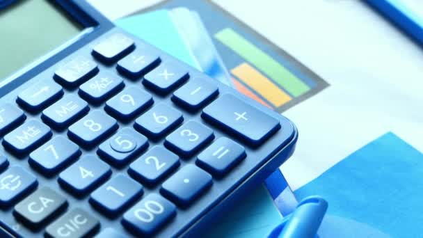 Zbliżenie niebieskiego kalkulatora i wykres finansowy na stole. — Wideo stockowe