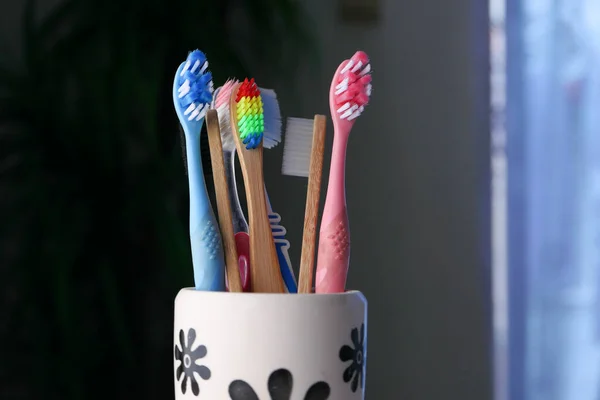 Spazzolini da denti colorati in tazza bianca contro un muro — Foto Stock