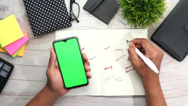 Man hand holding smart phone en het schrijven van wekelijkse planner — Stockvideo