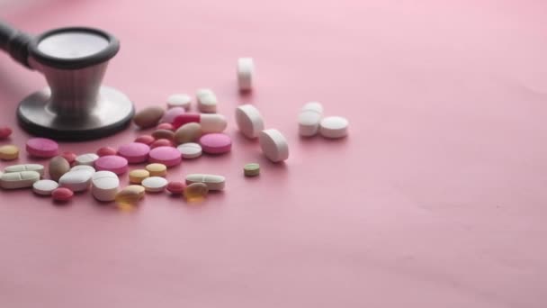 Közelkép színes tabletták és sztetoszkóp rózsaszín háttér — Stock videók
