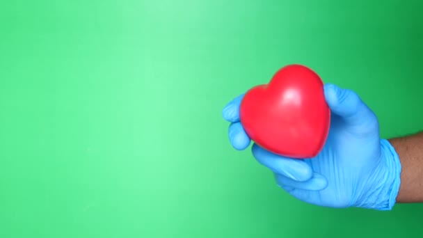 Médico mano en guantes médicos sosteniendo el corazón rojo sobre fondo verde — Vídeo de stock