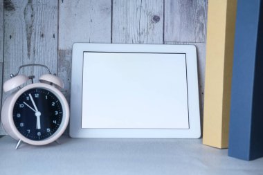 Boş ekran, saat ve kitap yığınına sahip dijital tablet 