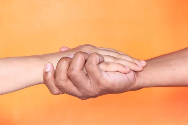 Nahaufnahme eines Paares, das sich vor orangefarbenem Hintergrund an den Händen hält. — Stockfoto