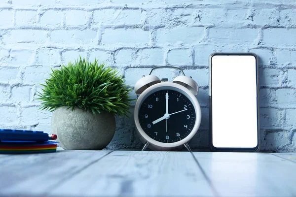 alarm clock, notepad and smart phone with empty screen on table