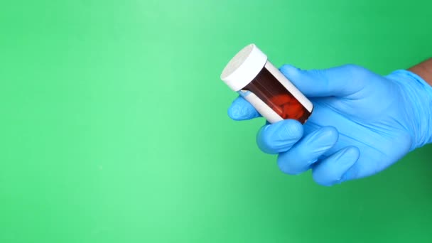 Ręka lekarza z rękawiczkami medycznymi trzymającymi pojemnik na pigułki przeciwko zielonemu ekranowi — Wideo stockowe