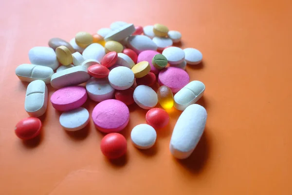 Primo piano di pillole colorate versando su sfondo arancione — Foto Stock