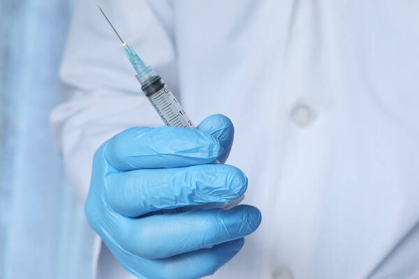 Врач в медицинских перчатках с шприцем в руках.