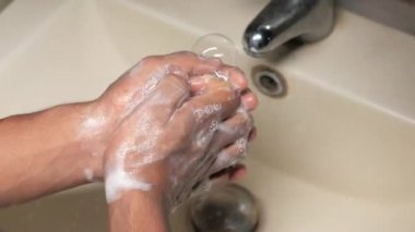 Genç adam ellerini sabunla sıcak suyla yıkıyor. 