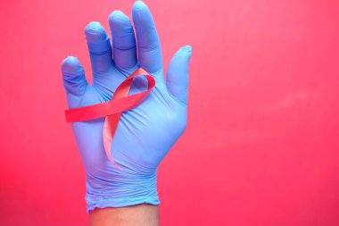 Kırmızı arka planda kırmızı HIV kurdelesini tutan el aşağı doğru 