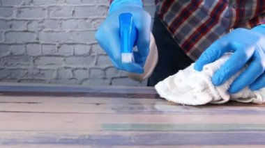 Elinde sprey şişesi ve temizlik masası tutan mavi lastik eldivenler. 