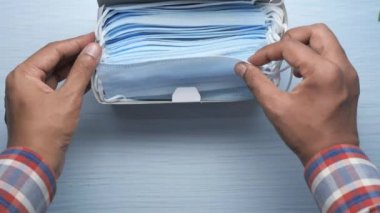 Bir kutudan cerrahi maske çıkartan bir adamın el görüntüsü. 