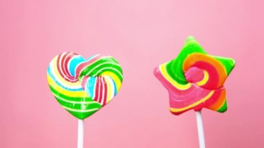 Pembe arka planda el ele tutuşan kalp şeklinde lolipop.,