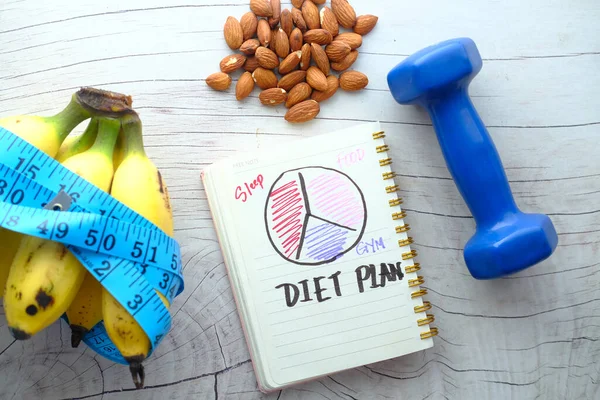 Diet rencana dengan kacang almond, dumbbells, pisang di atas meja . — Stok Foto