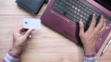Adamın elleri kredi kartını tutuyor ve internetten bilgisayar alışverişi yapıyor. 
