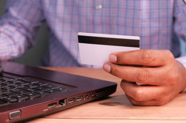 Adamın elleri kredi kartını tutuyor ve internetten bilgisayar alışverişi yapıyor. 