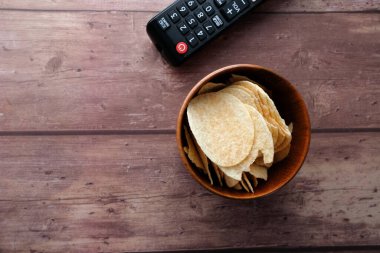 Tahta arka planda bir kase cips ve uzaktan kumanda. .