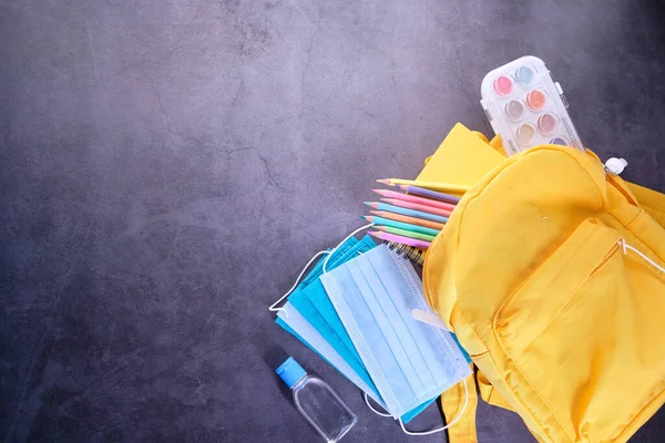 Sac à dos jaune, papeterie, masque et désinfectant sur fond noir — Photo