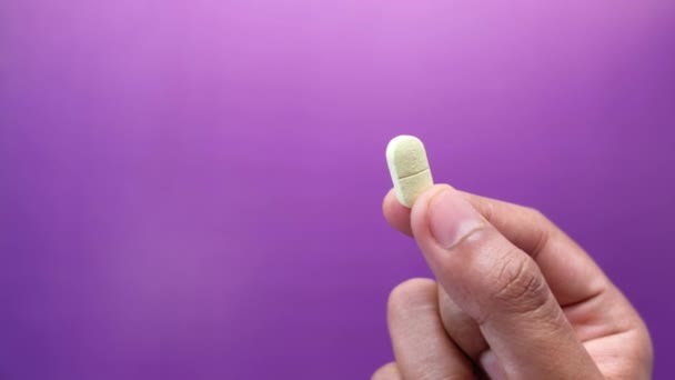 Hand hält Pillen auf lila Hintergrund mit Kopierraum — Stockvideo