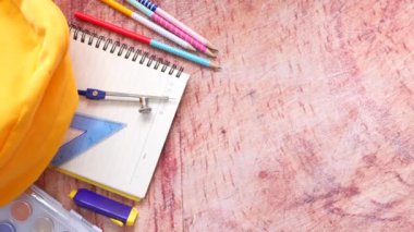 Masada farklı renkte kırtasiye malzemesi olan sarı sırt çantasının üst görünümü.